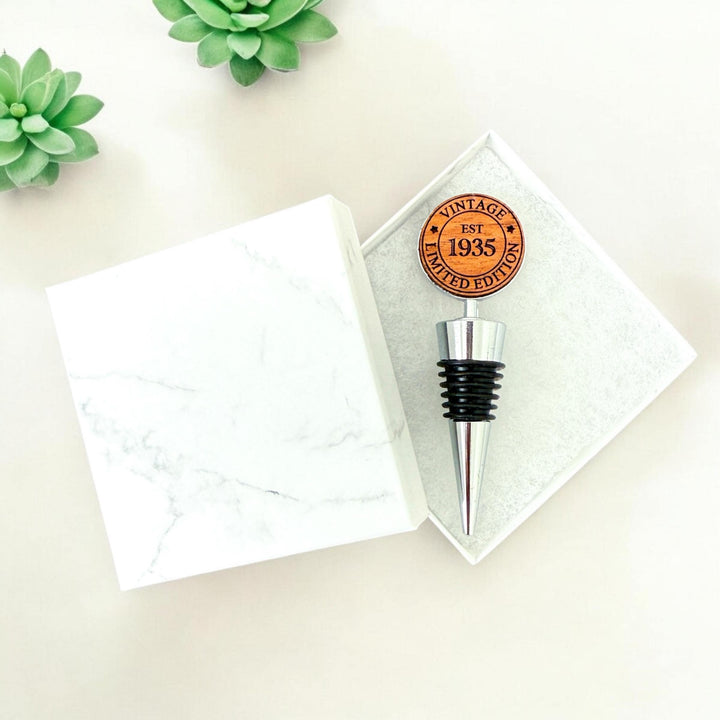 Double sided personalized wooden wine stoppers for a 90th birthday, engraved with &quot;Vintage Limited Edition EST 1935&quot; design.  Ideal for milestone birthday celebrations and wine lovers. Custom wine stopper shown in white marble gift box.