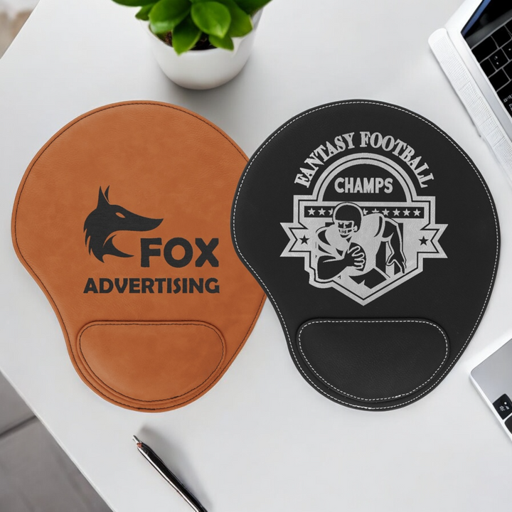 Two custom laser engraved leatherette mouse pads with wrist support, displayed in tan and black featuring corporate logos. Made from durable, water-resistant leatherette, these ergonomic mouse pads are perfect for corporate branding, promotional gifts, or personalized desk accessories.