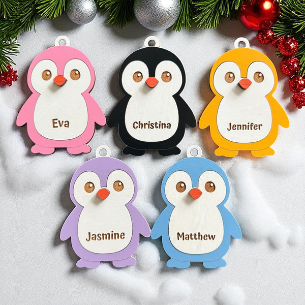 Custom personalized penguin ornament made from layered wood, available in pink, black, yellow, purple, and blue, engraved with any name for a unique Christmas decoration or family gift.