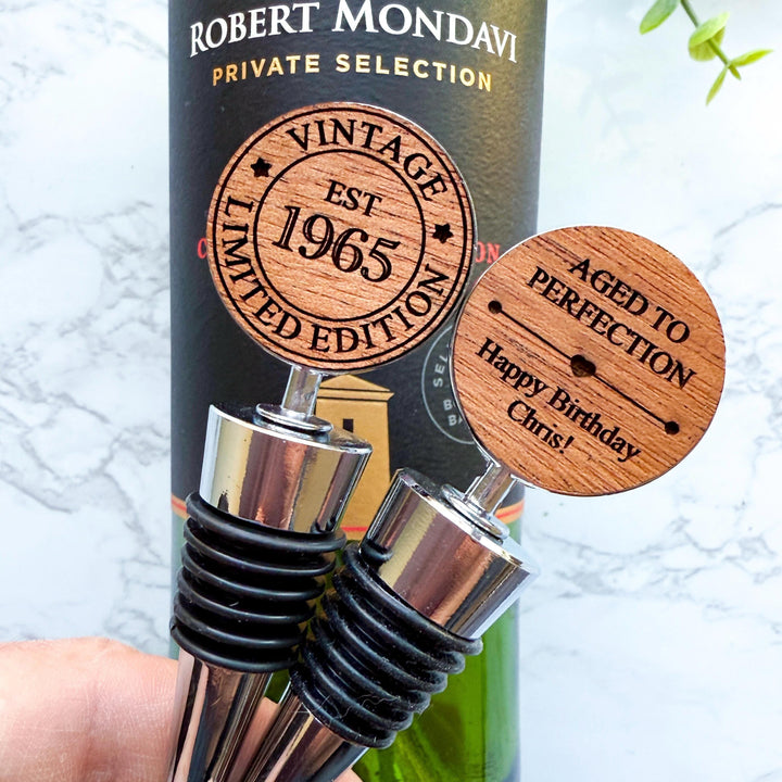 Personalized double sided wooden wine stoppers for a 60th birthday displayed in front of a wine bottle. Perfect custom gift for milestone birthday and wine enthusiasts.