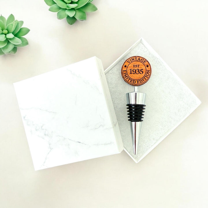 Double sided personalized wooden wine stoppers for a 90th birthday, engraved with &quot;Vintage Limited Edition EST 1935&quot; design.  Ideal for milestone birthday celebrations and wine lovers. Custom wine stopper shown in white marble gift box.