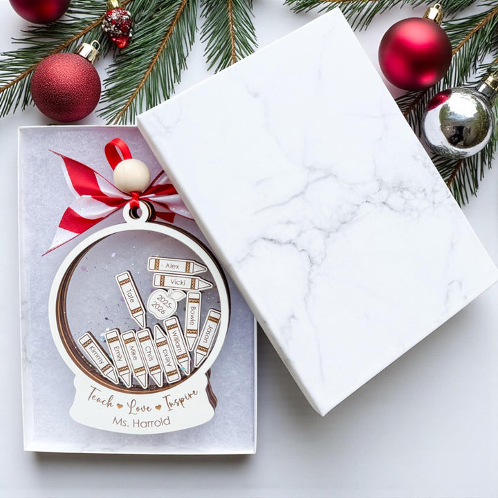 Flat lay of personalized teacher ornament inside marble gift box with red bow and Christmas ornaments around. Showcases packaging and gift-ready presentation for custom teacher gift.